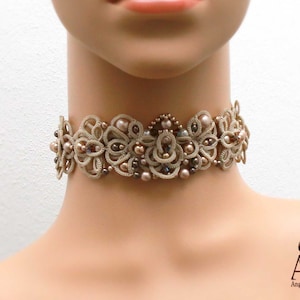 Pode incluir: Um delicado colar de renda bege com contas marrons e bege. O colar é feito de renda de crochê intrincada e apresenta um design floral.