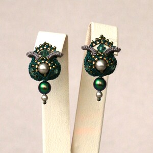 May include: A pair of green and silver beaded earrings with a pearl and a green iridescent bead hanging from each earring.