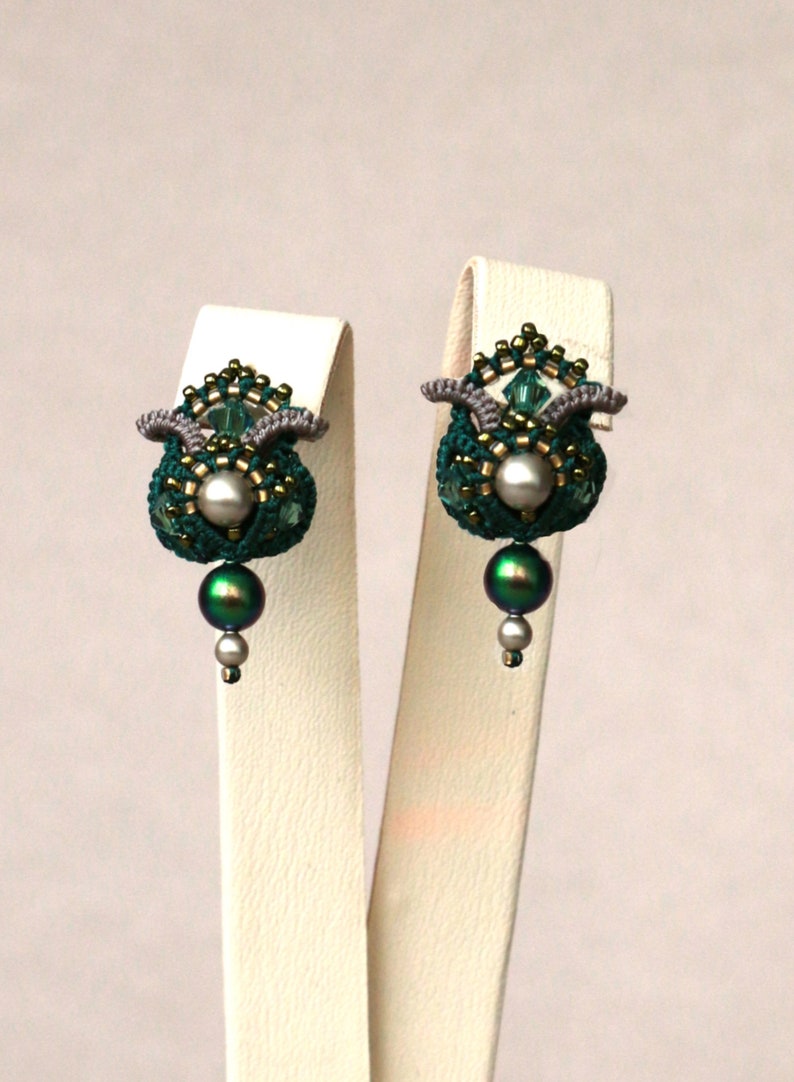 May include: A pair of green and silver beaded earrings with a pearl and a green iridescent bead hanging from each earring.