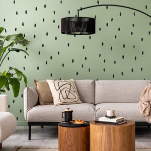Könnte beinhalten: Modernes Wohnzimmer mit hellgrauem Sofa, zwei hölzernen Beistelltischen und einer schwarzen Bogenstehleuchte. Dekorative Kissen und eine Decke sorgen für Textur. Die Wand ist hellgrün mit schwarzen Tupfenakzenten.