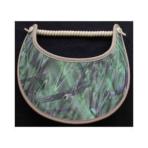 May include: A green and purple camouflage patterned visor with a beige trim and a beige rope strap.