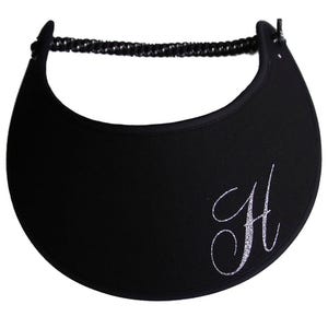 May include: Black visor with a curved brim and a black elastic band. The visor features a silver glitter cursive letter "H" on the front. This sun visor is designed to shield the eyes from the sun.