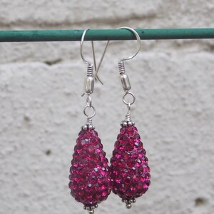 May include: A pair of dangle earrings with teardrop-shaped pink crystal beads. The earrings are made of silver and have a hook closure.