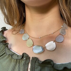 May include: A layered necklace with a gold chain and multiple oval-shaped pendants. The pendants are made of a pearlescent material and have a subtle shimmer.
