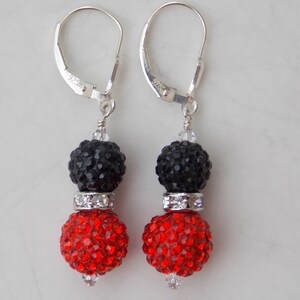 May include: A pair of dangle earrings with black and red crystal beads. The earrings have silver hooks and a silver spacer bead between the two crystal beads.