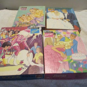 May include: Four rectangular Barbie jigsaw puzzle boxes featuring colorful illustrations of Barbie in various scenes, including a wedding, a rock concert, and a birthday party, with the Barbie logo clearly visible on the front of each box.