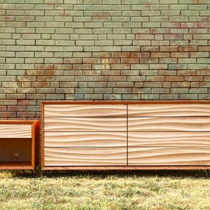 May include: A set of two wooden dressers with a wavy carved design. The larger dresser has six drawers and the smaller dresser has one drawer. Both dressers have black metal hairpin legs.