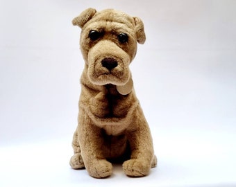 May include: A brown plush toy dog with a wrinkled face and floppy ears. The dog is sitting with its paws tucked under its body and is looking directly at the camera.