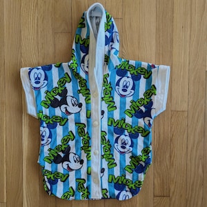 May include: A white hooded towel with blue and green stripes and a Mickey Mouse print. The towel has a button closure.