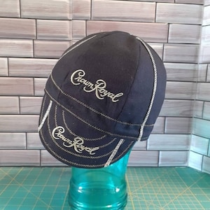 May include: Black Crown Royal branded welding cap with gold embroidery. The cap has a brim and a seam down the center of the crown.
