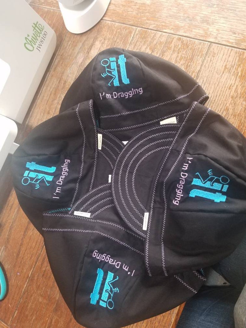 May include: Four black welding caps with a blue embroidered design of a stick figure dragging a toilet. The text "I'm dragging it" is embroidered on each cap.