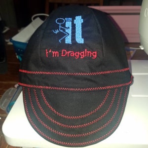 May include: A black and red baseball cap with a blue and white embroidered design that says "I'm Dragging It".