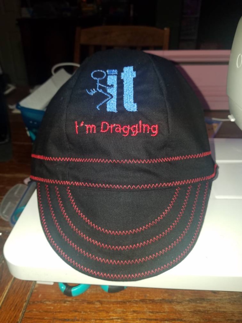 May include: A black and red baseball cap with a blue and white embroidered design that says "I'm Dragging It".