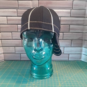 May include: A black cycling cap with white and yellow stitching. The cap is on a blue mannequin head.