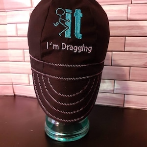 May include: Black welding cap with a turquoise stick figure and the text "I'm Draggling" embroidered on the front.