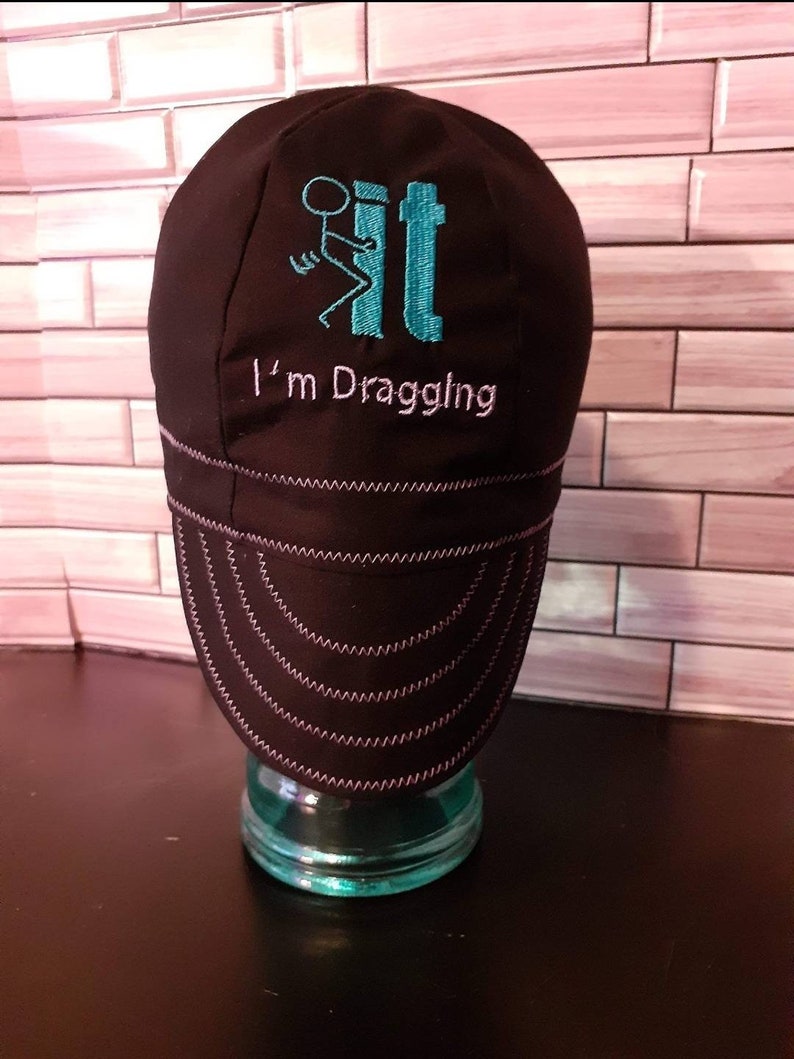 May include: Black welding cap with a turquoise stick figure and the text "I'm Draggling" embroidered on the front.