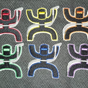 May include: Six embroidered patches in different colors, each featuring a stylized figure with a welding mask and a lasso. The patches are black with white outlines and feature different colored accents.