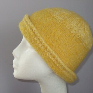 May include: A yellow knitted hat with a wide brim. The hat is made of a soft, fuzzy yarn and has a simple, classic design.