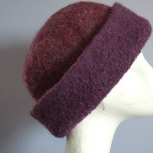 May include: A purple and burgundy wool hat with a wide brim. The hat is made of a soft, textured fabric.