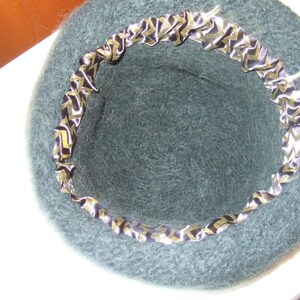 May include: A dark green felt hat with a black and gold patterned ribbon around the brim.