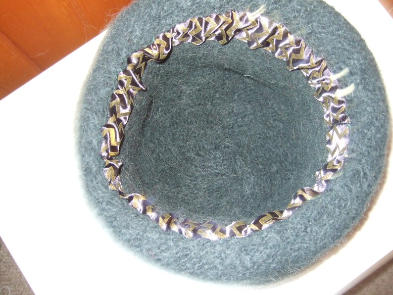 May include: A dark green felt hat with a black and gold patterned ribbon around the brim.