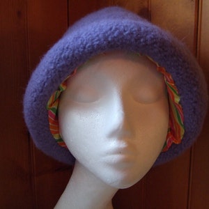 May include: A purple fuzzy hat with a colorful striped lining. The hat is worn on a white mannequin head.
