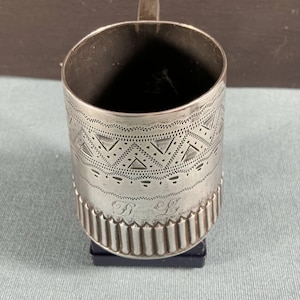 May include: A silver cup with a geometric pattern and the initials "D.L." engraved on the bottom.