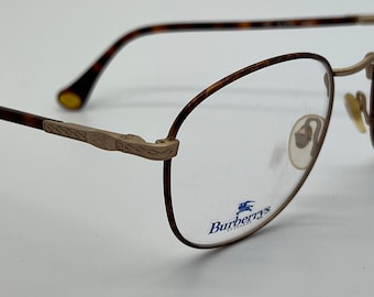 May include: A pair of gold-rimmed glasses with tortoise shell arms. The glasses have clear lenses and the Burberry's logo is printed on the right lens.