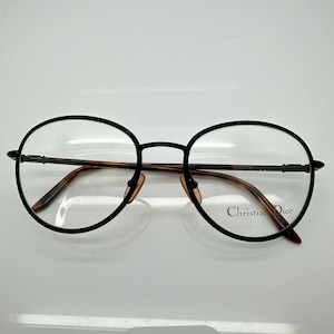 May include: Black metal framed eyeglasses with round lenses. The brand name "Christian Dior" is printed on the right temple.