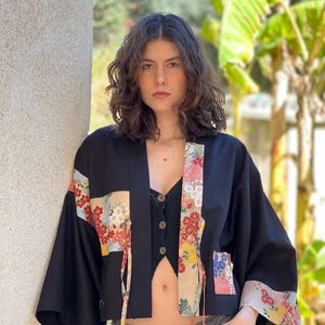 May include: A black cropped kimono jacket with floral patterned fabric accents. The jacket has long sleeves and a tie closure at the front.