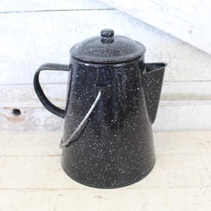 May include: Black enamel coffee pot with white speckles, featuring a lid and handle. The vintage-style pot has a spout for pouring and a wire handle. A classic kitchenware item.