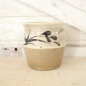 May include: A ceramic planter with a brown and white glaze. The planter has a black floral design on the top half.