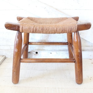 May include: A wooden stool with a woven rush seat. The stool has a simple design with four legs and a single stretcher.