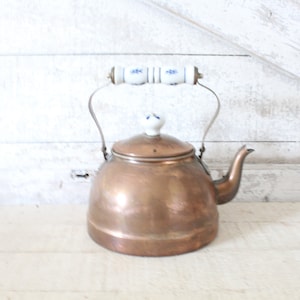 May include: A copper kettle with a white porcelain handle and lid. The kettle has a blue and white floral design on the handle and lid.