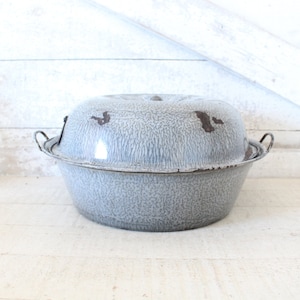 May include: A vintage gray enamelware covered casserole dish with two handles. The dish has a speckled gray and white finish with brown accents.