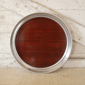 May include: A round silver tray with a dark wood center. The tray has a beaded edge and is perfect for serving snacks or drinks.