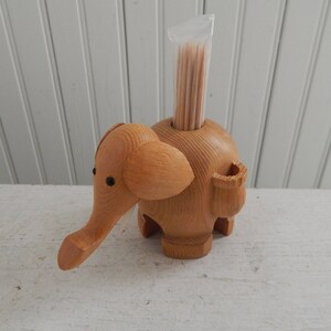 Puede incluir: Porta palillos de dientes de madera con forma de elefante con un recipiente de pl&aacute;stico transparente en la parte superior lleno de palillos de dientes.