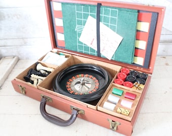 May include: A vintage brown suitcase-style game set, open to reveal a roulette wheel, chess pieces, dice, and poker chips. The interior features a green felt game board and various compartments for game components.