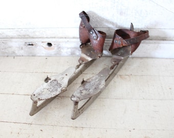 May include: A pair of vintage ice skates with leather straps and metal blades. The skates are in good condition and have a rustic look.