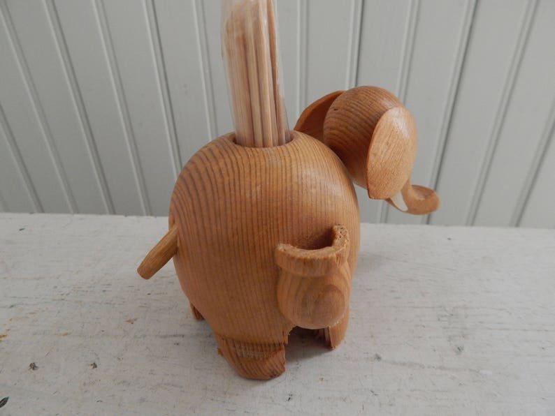 Puede incluir: Porta palillos de dientes de madera en forma de elefante con un acabado de madera natural. El elefante tiene una trompa larga y una cola peque&ntilde;a. El soporte est&aacute; dise&ntilde;ado para sostener los palillos de dientes en posici&oacute;n vertical.