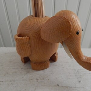 Puede incluir: Porta palillos de dientes de madera con forma de elefante con una ranura para los palillos en el lateral. El elefante est&aacute; hecho de madera marr&oacute;n claro y tiene ojos negros.