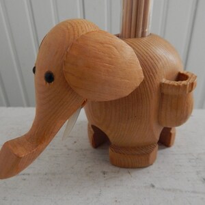 Puede incluir: Porta palillos de dientes de madera con forma de elefante con una ranura para palillos en el lateral. El elefante es marr&oacute;n y tiene ojos negros.