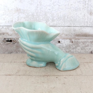May include: A light blue ceramic hand-shaped planter with a flower-shaped opening. The planter is designed to look like a hand holding a flower.