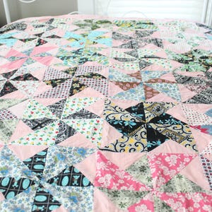 May include: A handmade quilt with a pinwheel design. The quilt features a patchwork of various fabrics in shades of pink, blue, green, black, and white. The quilt is on a bed with a white headboard.