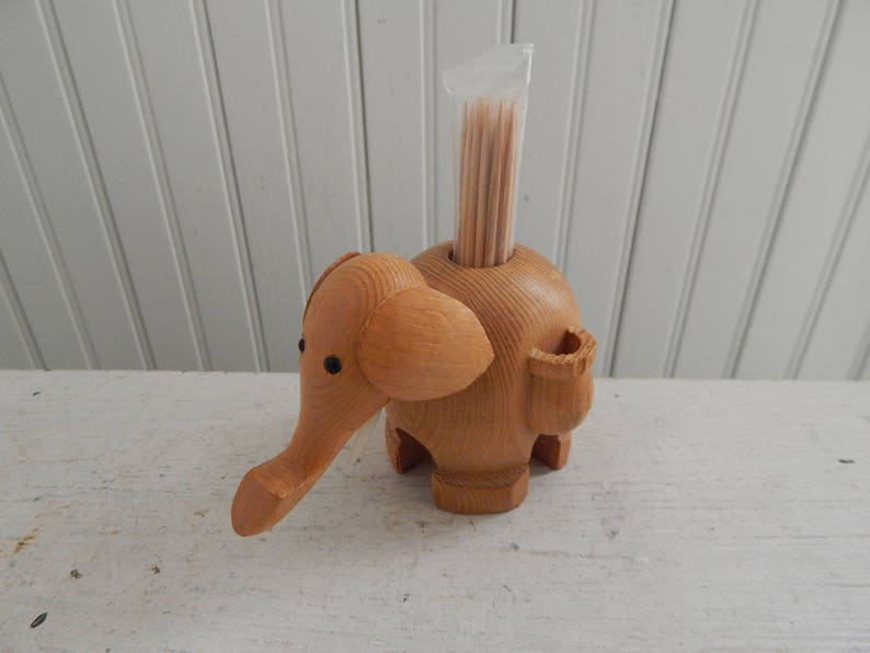 Puede incluir: Porta palillos de dientes de madera con forma de elefante con un recipiente de pl&aacute;stico transparente en la parte superior lleno de palillos de dientes.