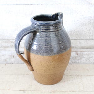 May include: A handmade ceramic pitcher with a blue and brown glaze. The pitcher has a wide mouth and a handle.
