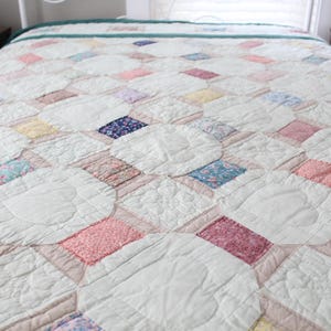 May include: A handmade quilt with a repeating pattern of white circles and colorful squares. The squares are in shades of pink, blue, purple, and yellow. The quilt is on a bed, and the overall aesthetic is vintage and cozy.
