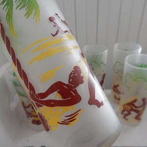 K&ouml;nnte beinhalten: Set aus mattierten Gl&auml;sern mit tropischem Insel-Motiv. Die Gl&auml;ser zeigen eine braune Silhouette einer Person auf einem Surfbrett mit einer Palme und gelben Wellen im Hintergrund.