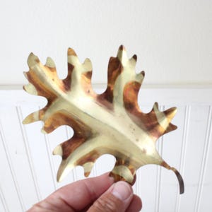 May include: A gold-toned metal leaf with a textured surface. The leaf has a brown and gold color pattern.