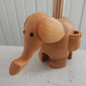 Puede incluir: Porta palillos de dientes de madera en forma de elefante con ojos negros. El elefante tiene un peque&ntilde;o compartimento en el lateral para los palillos de dientes.